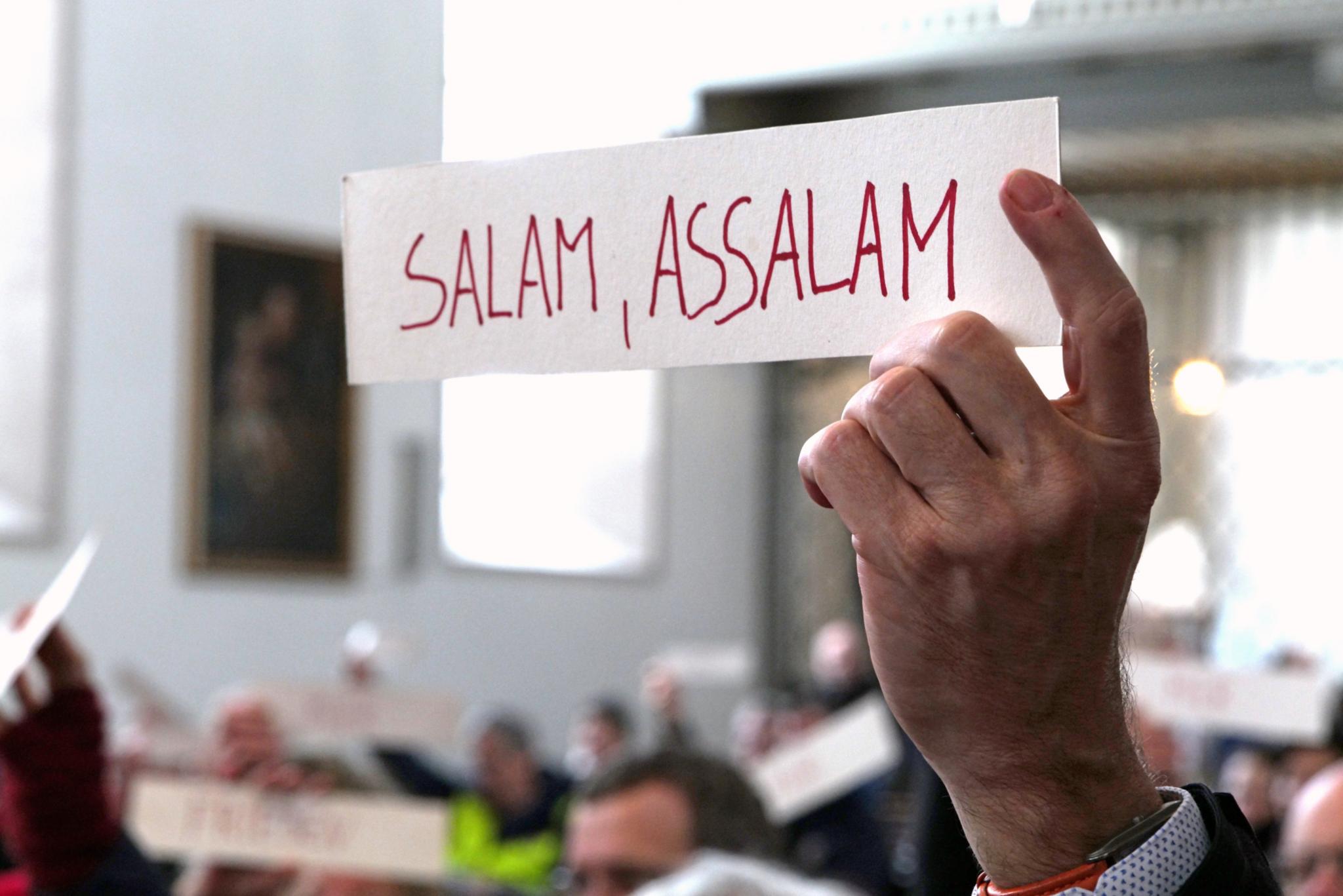 Hand hält Schild mit der Aufschrift 'Salam, assalam'