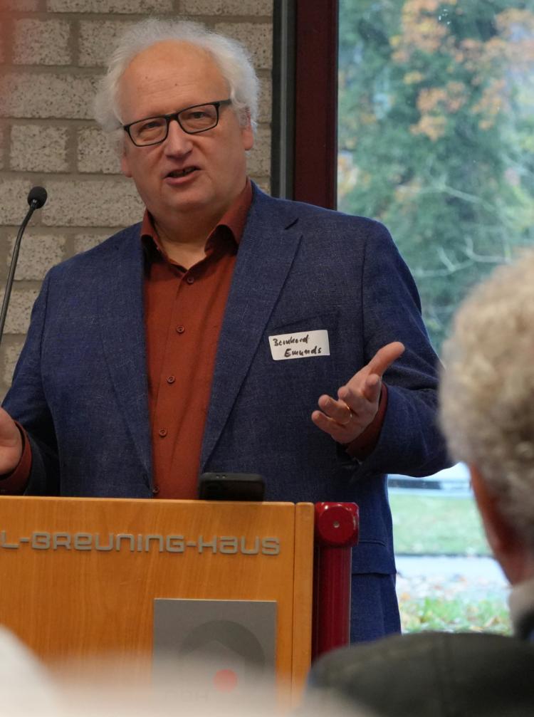 Ein Mann spricht am Rednerpult zu Menschen und hebt dabei die Hände.