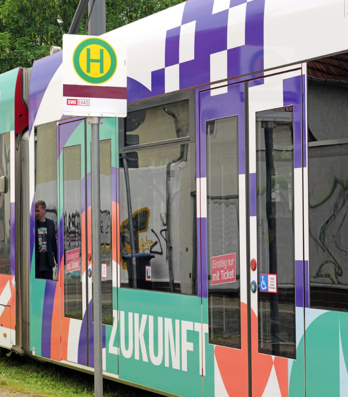 Das Bild zeigt eine Straßenbahn, die an einer Haltestelle steht und den Schriftzug 'Zukunft' trägt.