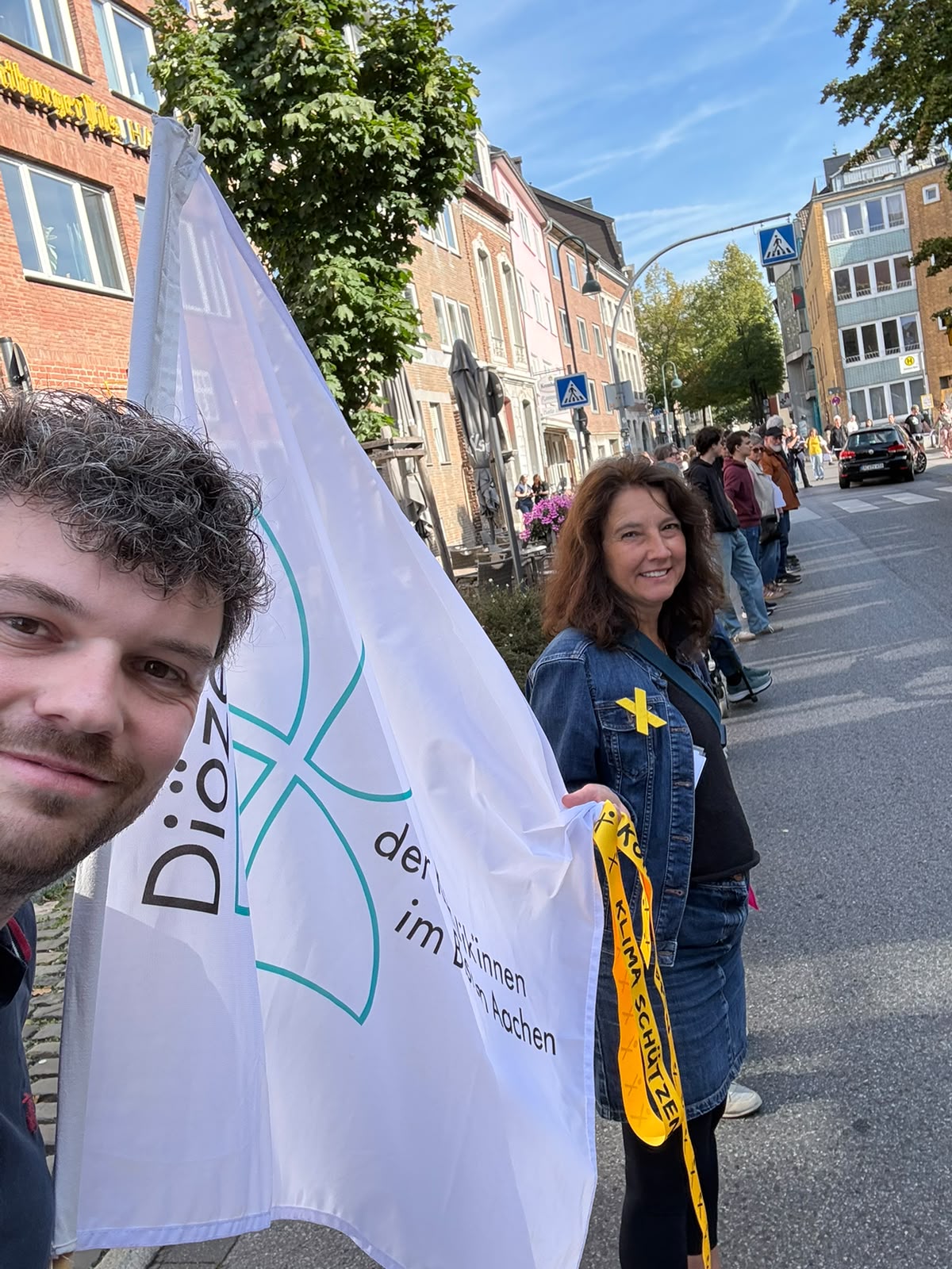 Matthias Follmann und Marie-Theres Jung stehen mit der Flagge des Diözesanrats Aachen in der Menschenkette.