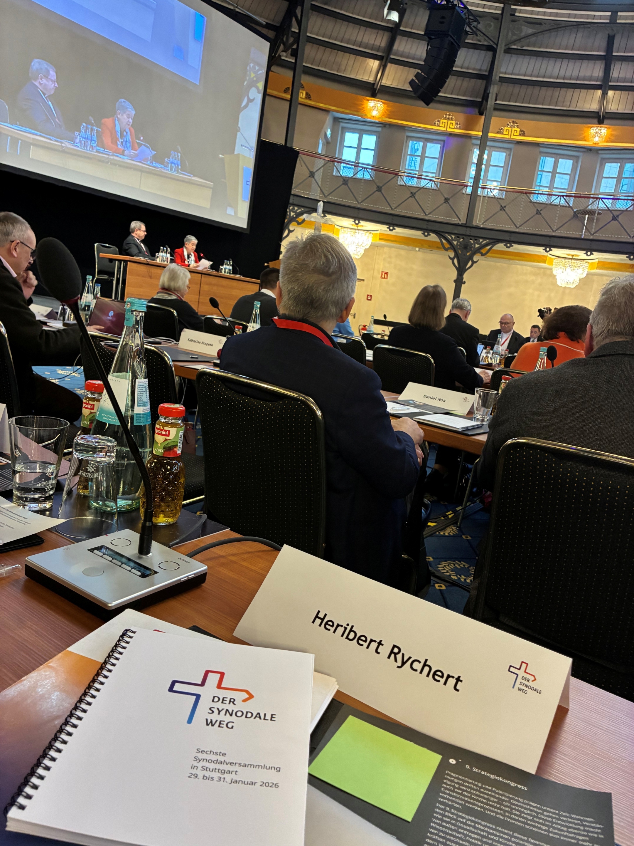 Ein Saal mit Sitzungsunterlagen und Menschen.